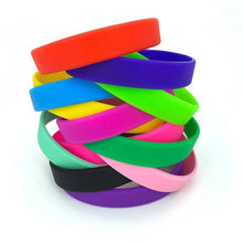 A stack of colorful silicone wristbands in red, purple, blue, yellow, green, pink, black, and light pink, arranged on a plain white background.