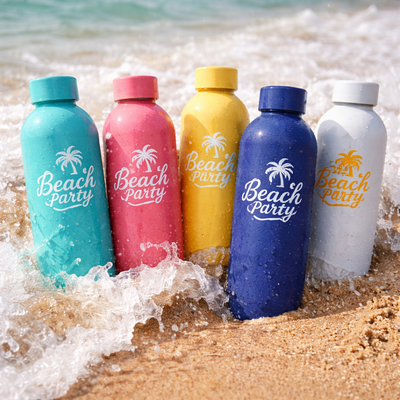 Five colorful Custom Printed Stainless Steel Water Bottles with 'Beach Party' text on a sandy beach with ocean waves.