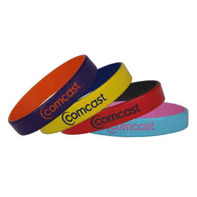 Four silicone wristbands in orange, purple, yellow, black, red, and light blue, each printed with the Comcast logo, arranged in a fan shape on a white background.