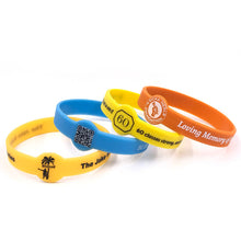 Four silicone wristbands in orange, yellow, and blue, arranged in a fan shape on a white background. Each band features custom printed designs, including text, QR codes, and a palm tree charm.