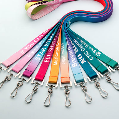 A fanned-out display of colorful fabric lanyards with metal swivel clips on a light gray background. The lanyards come in multiple colors including pink, purple, red, blue, teal, orange, and light blue, with white printed text and logos.