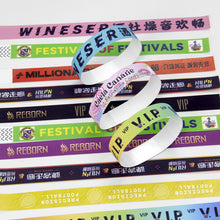 A stack of colorful custom printed wristbands with text such as 'VIP', 'FESTIVAL', 'MILLENNIALS', 'REBORN', and 'WINESER', photographed on a plain white background.