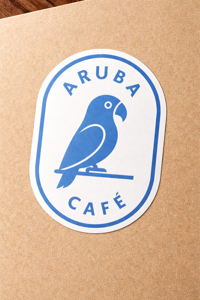 Sticker with a parrot design and 'Aruba Café' text on a brown paper background