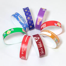 A set of colorful paper wristbands arranged in a circle on a white background. The wristbands come in multiple colors including blue, purple, green, red, orange, and maroon, each printed with various logos and text.