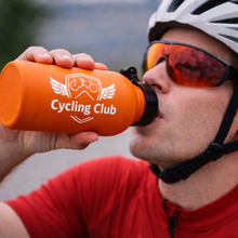 Person in cycling gear drinking from an orange 'Cycling Club' water bottle.