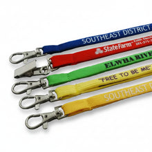Five Custom Tubular lanyards in blue, red, green, yellow, and orange, each with a silver lobster clasp and printed with State Farm branding and district text, arranged diagonally on a gray surface.